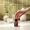 Hand placing an essential oil bottle on a bathroom counter with soft natural lighting.