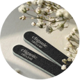 Two black nail files with white 'Chicory' branding, shown inside a circular frame with dried baby's breath flowers on a light beige background.