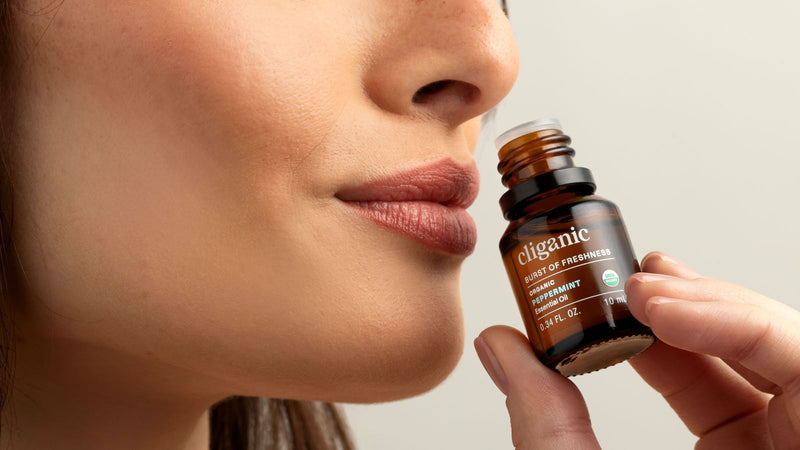 Person holding a bottle of cliganic peppermint essential oil near their face.