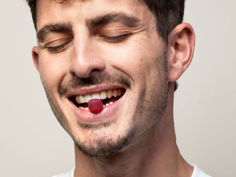 Man holding a gummy between his teeth on a plain background