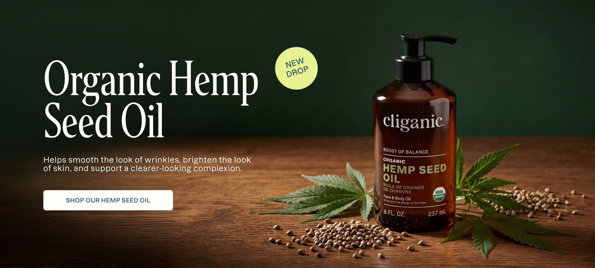Cliganic organic hemp seed oil bottle on a wooden surface with leaves and seeds.